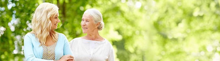 Seniorin und Pflegerin bei einem Spaziergang im Grünen.